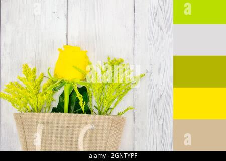 Gelbe Rose und Laub in einer hessischen Einkaufstasche flach lag auf Holz Hintergrund mit Farbthema Stockfoto