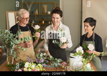 Waist-up-Porträt von drei kreativen Floristen, die in der Werkstatt Blumenkompositionen aufziehen Stockfoto