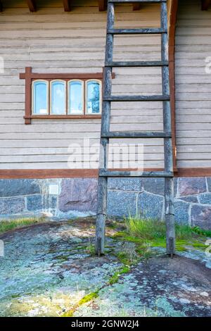 Helsinki / Finnland - 28. SEPTEMBER 2021: Holzleiter, die an der Außenseite eines alten Hauses mit einem Steinfundament und einem rustikalen karierten Fenster angelehnt ist Stockfoto