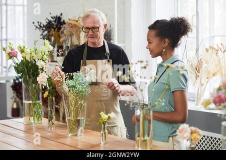 Porträt eines älteren Mannes, der während der Arbeit im Blumenladen eine junge Frau berät Stockfoto