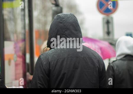 Menschen von hinten im Regen. Kapuzen gehen in Richtung Bus. Draußen regnet es. Schlechtes Wetter für die Menschen. Stockfoto