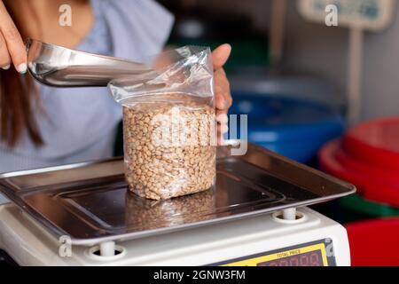 Frau, die Linsen in einen Beutel verpackt und mit Waage. Frau mit Metalllöffel, um Körner zu packen. Trockenkornlager. Stockfoto