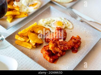 Gebackene Kartoffeln mit Huhn in Sauce und Spiegelei auf dem Teller Stockfoto