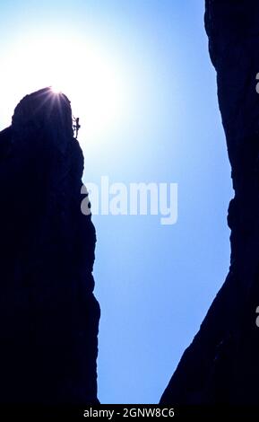 Eine Klettererin, die sich der Spitze einer Felsformation nähert, wo die Sonne ihren Höhepunkt erreicht. Stockfoto