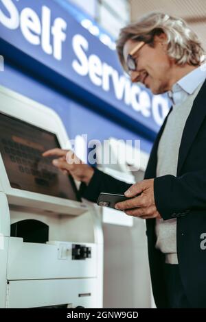 Aus der Perspektive eines Mannes, der am Flughafen einen Check-in-Automaten nutzt. Ein reifer Geschäftsmann, der am Flughafen eingecheckt hat. Stockfoto