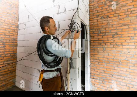 Reparaturdienst in Overalls mit Werkzeuggürtel im Gebäude stehend, Renovierung im Büro Stockfoto