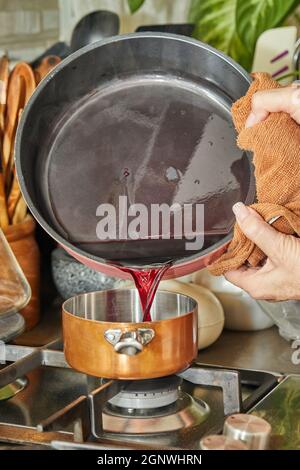 Der Koch gießt die Flüssigkeit in den Kupfertopf bei geringer Hitze auf den Herd, um die Sauce zu machen Stockfoto