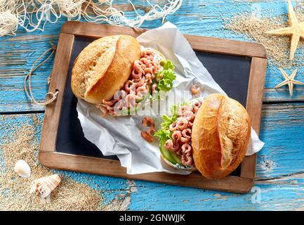 Blick von oben auf köstliche Sandwiches mit frischen, knusprigen Brötchen, gefüllt mit Garnelen und frischen Gurken und Salat, serviert auf einem Holztablett auf dem Tisch Stockfoto