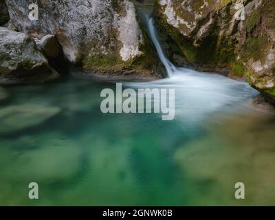 Kleiner Fluss tief in den grünen Wäldern. Wunderbare Frühlingsszenerie der Berglandschaft. Klares Wasser zwischen Wald und felsigen Ufer. Holzzaun an Stockfoto