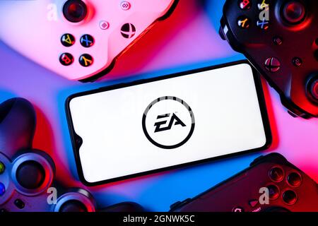 Ein Smartphone mit dem Electronic Arts-Logo auf dem Bildschirm, umgeben von Gamepads. Stockfoto