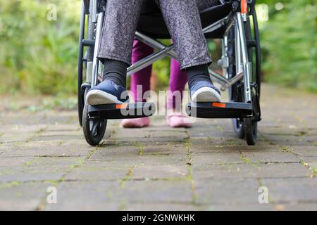 Ältere Frau im Rollstuhl, die mit der Pflegekraft läuft Stockfoto