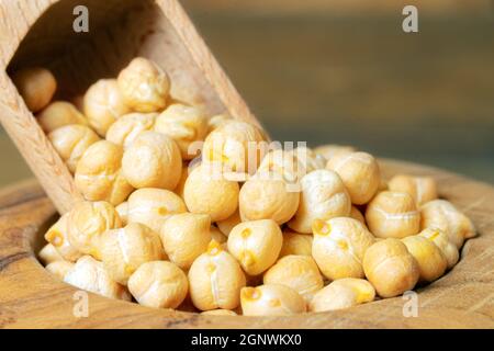 Nahaufnahme von Kichererbsen in einer Schüssel mit einer Schaufel. Getrocknete Kichererbsen in einer Holzschüssel auf Holzboden. Stockfoto