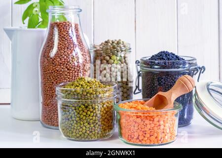 Sortiment an bunten Hülsenfrüchten in Gläsern und Gläsern auf einem hellen Küchentisch. Stockfoto