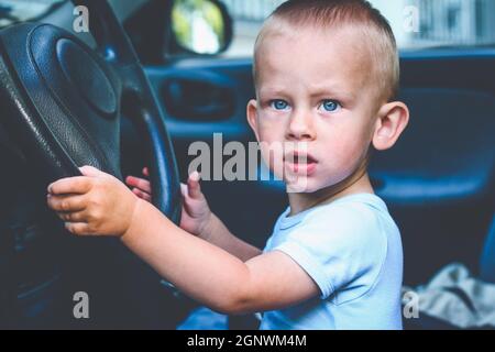 Ein einjähriger Junge sitzt hinter dem Steuer und gibt vor, Auto zu fahren Stockfoto