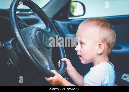 Ein einjähriger Junge sitzt hinter dem Steuer und gibt vor, Auto zu fahren Stockfoto