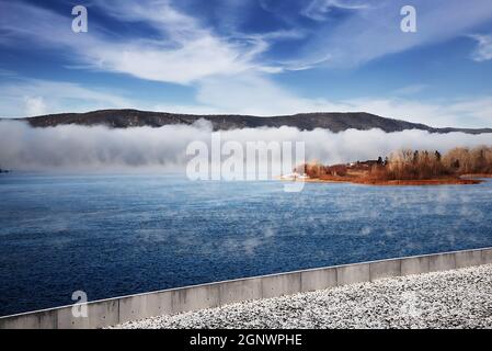 Winter frostiger Nebel auf einem ungefrorenen Fluss. Bäume und Gras am Ufer. Landschaft Natur. Stockfoto
