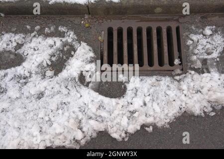 1 - Ansicht von oben von einem Highway Bordkantside Drain, auch bekannt als Surface Drain, empfangen Wasser laufen weg von geschmolzenem Schnee. Eine Tarmac Straße im städtischen Bereich. Stockfoto