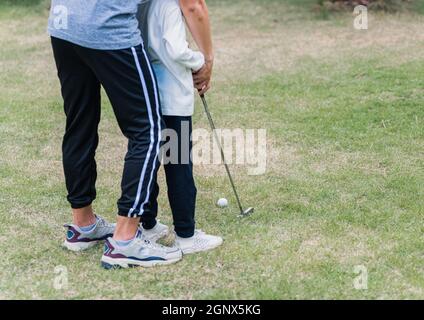 Asiatische junge Vater unterstützen Lehre Ausbildung Tochter zu spielen perfekte Golf, während im Spiel des Golfs zusammen in der Natur ein Feld Garten Park stehen, Stockfoto