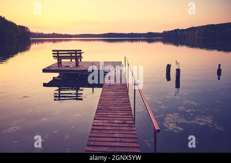 Hölzerner Seebrücke mit Bank bei Sonnenuntergang, Farbtonung aufgetragen. Stockfoto