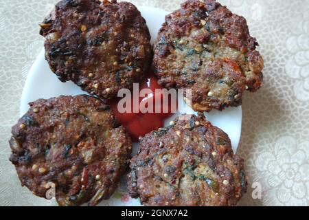 Köstlich würzig gebratener runder Kebab, serviert in weißer Keramikplatte auf einem Holzboden mit roter Sauce. Stockfoto