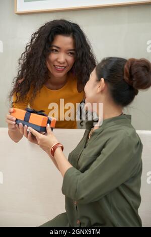 Lächelnde attraktive asiatische Frau, die der reifen Mutter eine Geschenkbox gibt, während sie ihr zum Geburtstag gratuliert Stockfoto
