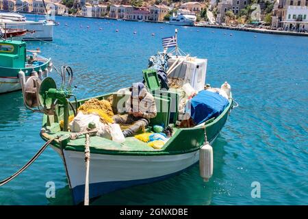 SYMI, Griechenland - 03. JUNI 2021. Ein traditionelles griechisches Fischerboot im Hafenviertel von Gialos auf der Insel SYMI. Der Fischer repariert oder repariert Stockfoto