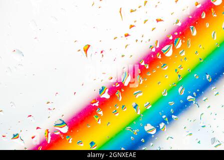 Ein Regenbogen hinter einem Glasfenster mit Wassertropfen, aus Sicht, hinter dem Glas mit Tropfen. Stockfoto