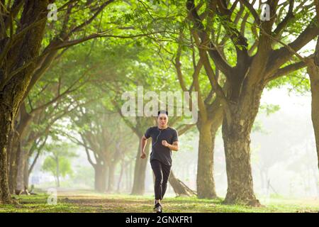Junger Mann, der durch den Park joggt und Musik hört Auf seinem Handy Stockfoto