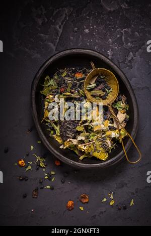 Mischung aus Tees, getrockneten Bio-Tee Kräuter und Früchte in Schüssel mit Tee-Sieb auf schwarzem Hintergrund Stockfoto