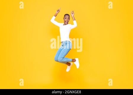 Energische junge afroamerikanische Frau, die mit nach oben zeigenden Händen im isolierten gelben Studiohintergrund springt Stockfoto