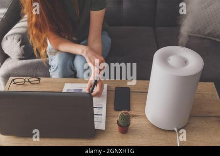 Freiberuflerin verwendet einen Hausbefeuchter am Arbeitsplatz im Heimbüro mit Laptop und Dokumenten. Stockfoto