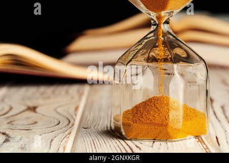 Sandglas auf Holztisch mit geöffnetem Buch aus nächster Nähe Stockfoto