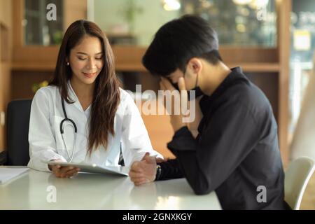 Schöne junge asiatische Ärztin ermutigt und erklärt einem männlichen Patienten den Operationsplan. Stockfoto