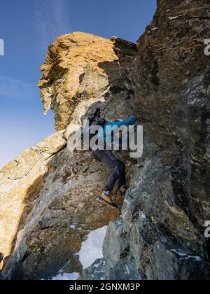 Rückansicht von Felskletterern mit Rucksäcken mit festem Seil beim Aufstieg auf einen hohen felsigen Berg. Männliche Bergsteiger klettern auf natürliche Felsformationen Stockfoto