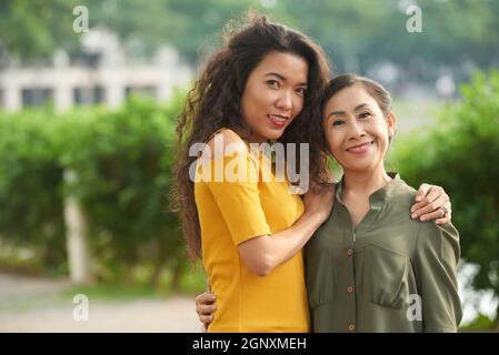 Portrait einer positiven erwachsenen vietnamesischen Tochter, die reife Mutter auf der Straße umarmt Stockfoto