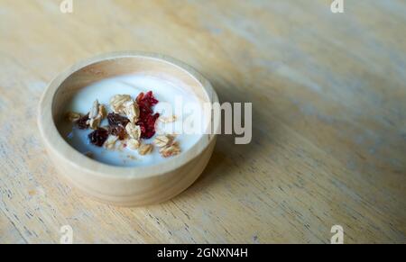 Getrocknete Früchte und Vollkornprodukte in einer Joghurtschale auf einem Holztisch. Stockfoto