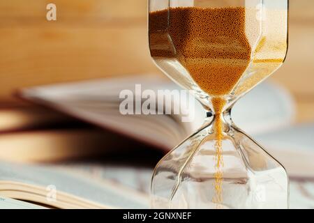 Sandglas auf Holztisch mit geöffnetem Buch aus nächster Nähe Stockfoto