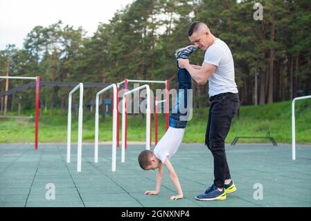 Kaukasischer Mann lehrt Sohn Handstand auf Spielplatz. Stockfoto