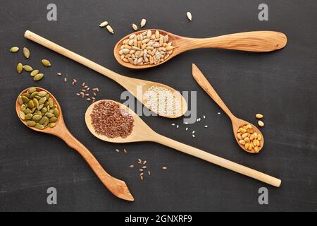 Verschiedene Sorten von Nüssen und Samen liegen in Holzlöffeln auf schwarzem Schiefergrund. Draufsicht. Gesunde Ernährung. Vegetarische Ernährung Stockfoto