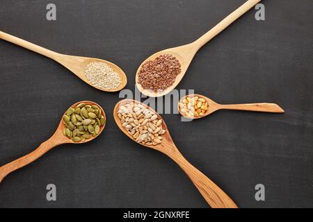 Verschiedene Sorten von Nüssen und Samen liegen in Holzlöffeln auf schwarzem Schiefergrund. Draufsicht. Gesunde Ernährung. Vegetarische Ernährung Stockfoto