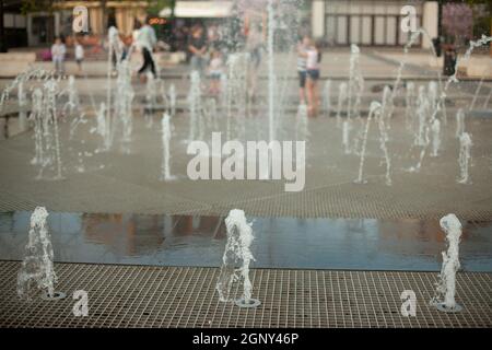 Stadtbrunnen auf dem Platz. Wasser sprudelt aus den Gehwegen. Flugzeugbrunnen in der Stadt. Spritzende Wasserspiele. Stockfoto