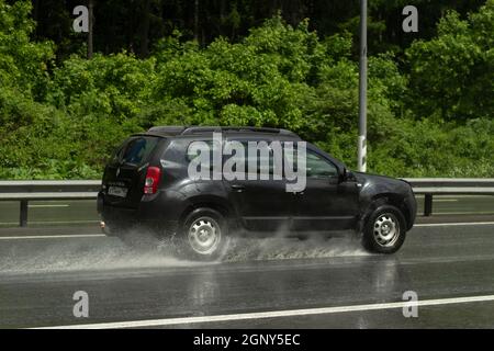 Das Auto fährt auf nasser Straße. Rutschige Straße nach Regen. Spritzer unter den Transporträdern. Regen auf der Autobahn. Sommerregen in den s Stockfoto