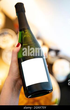 Junge Frau mit Champagner-Flasche mit leerem Etikett am Abendessen Stockfoto
