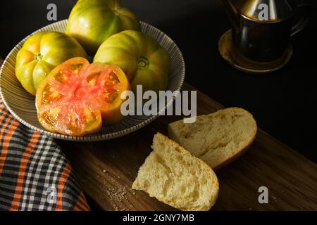 Tisch mit einem Teller mit mehreren Tomaten der Sorte Perelló Mascle (Macho), typisch für die Region Valencia, in Spanien, begleitet von einer Ölkälte mit Stockfoto