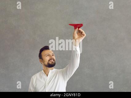 Ein glücklicher junger Mann, der ein Papierflugzeug als Metapher für den Erfolg wirft Stockfoto