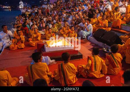 Zuschauer, Gläubige, Anhänger und Priester in orangefarbenen Gewändern in der heiligen Stadt Rishikesh in Uttarakhand, Indien während der abendlichen Lichtzeremonie cal Stockfoto