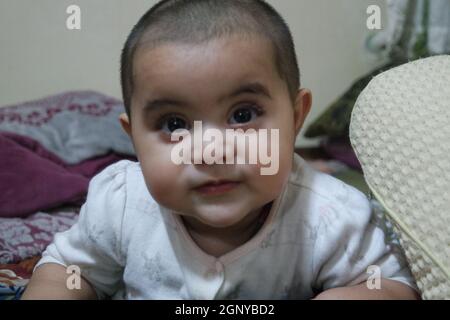 Baby-Mädchen mit schönen Gesicht, große Augen und niedliche Gesichtsgeste. Baby mit kahlem Kopf starrt auf die Kamera. Stockfoto