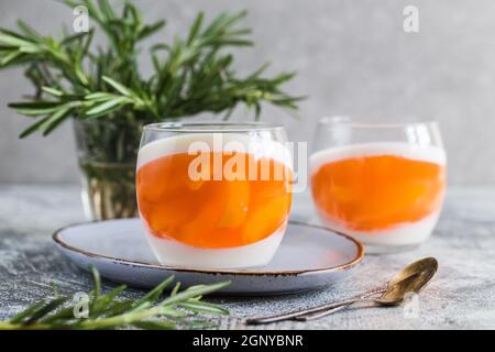 Hausgemachte Panna Cotta mit Scheiben von Pfirsich und Pfirsich Gelee in Glasgefäßen auf einem grauen Beton Hintergrund. Stockfoto