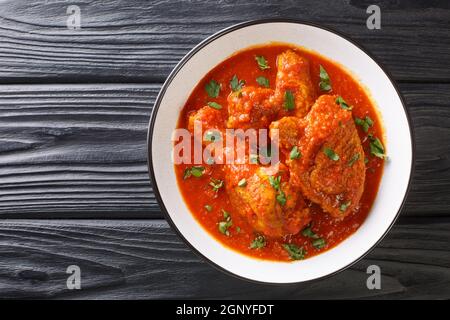 Ayam masak merah ist ein malaysisches Gericht mit Hühnerstücken, die in einer reichen, würzigen und cremigen Tomatensauce in einer Schüssel auf dem Tisch in der Nähe übergossen werden Stockfoto