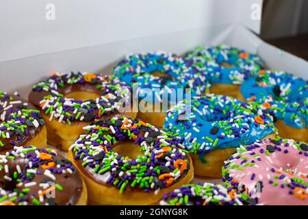 Donuts mit brauner, blauer, rosa und weißer Glasur, bedeckt mit bunten Streuseln in einer weißen Box auf einem Holztisch Stockfoto